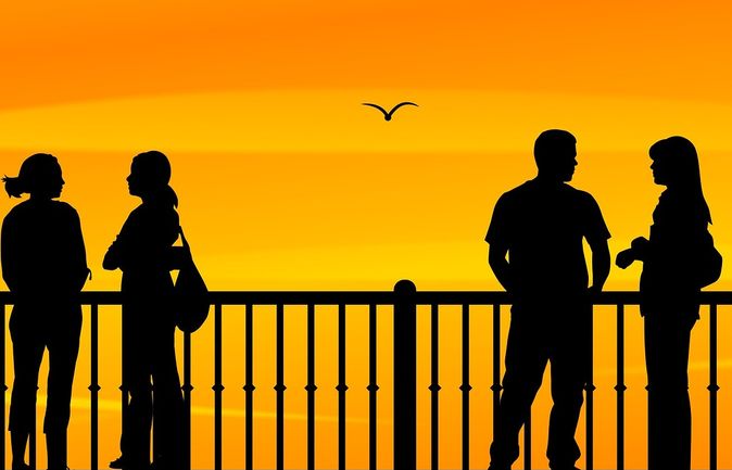 Silhouetten mehrerer Menschen in kleinen Gruppen auf Brüstung bei Sonnenuntergang