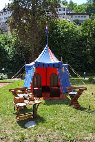 Blau-rotes Mittelalterzelt mit offenen Eingängen und Holzmöbeln