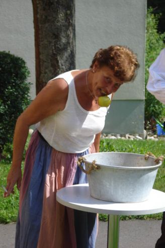 Frau beugt sich über Tisch und hat Apfel im Mund neben Zinkeimer