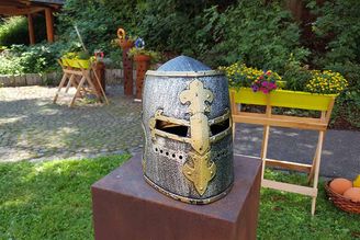 Mittelalterlicher Ritterhelm mit goldener Verzierung auf Podest