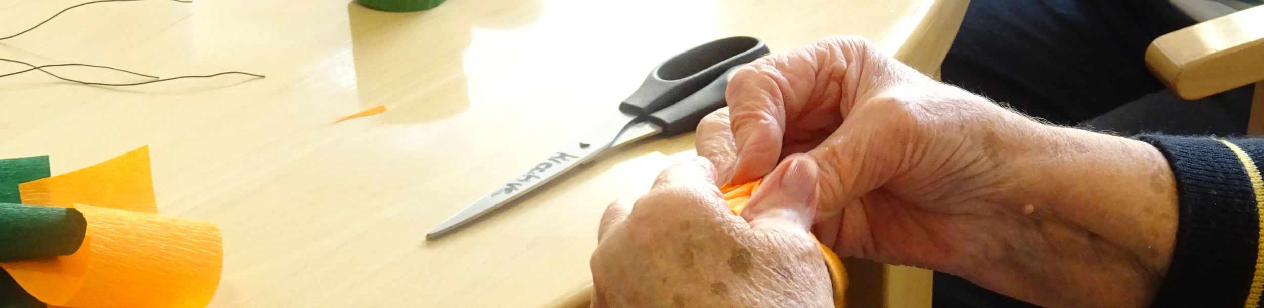 Hände falten orange Krepppapier neben Schere und Papierrollen