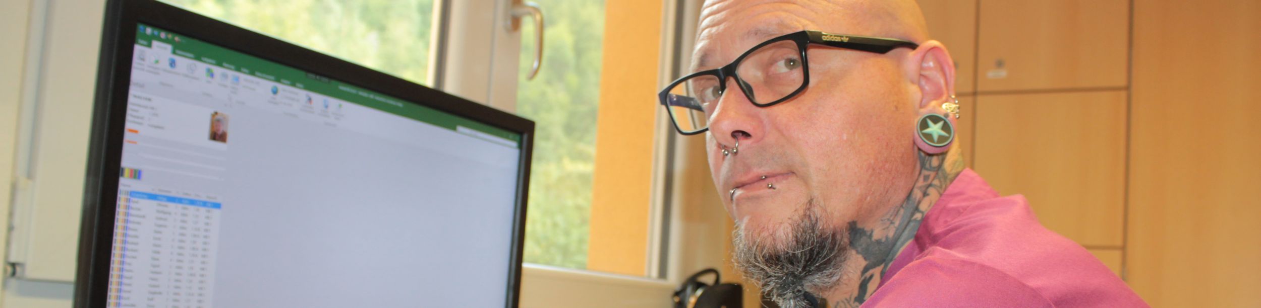 Tätowierte Person mit Piercings und großen Tunnel-Ohrringen am Computer