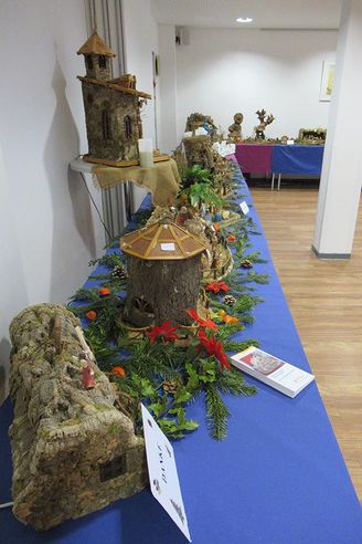 Ausstellung mit Miniaturlandschaften aus Baumrinde und Naturmaterialien auf blauem Tisch