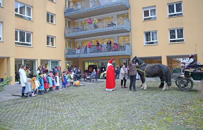 Kinder singen vor rot gekleideter Nikolaus neben Pferdekutsche im Wohnhof