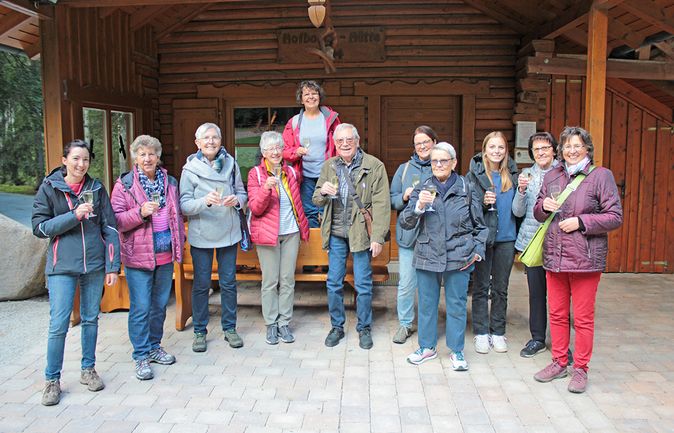 Wandergruppe prostet mit Gläsern vor Holzhütte zum Dankeschön