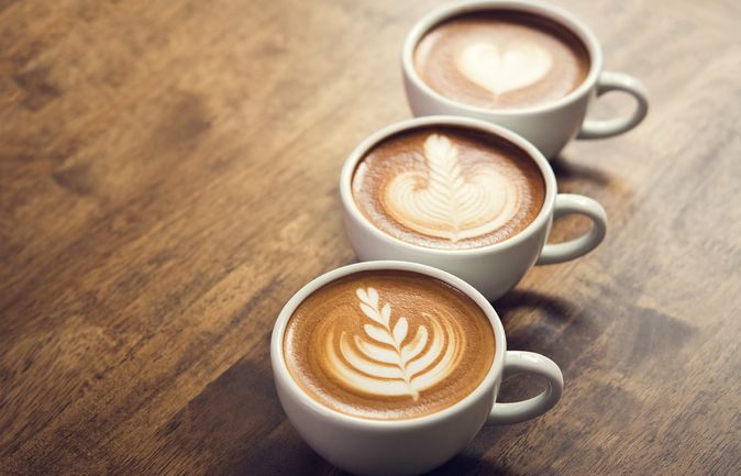 Drei Tassen Kaffee mit Latte‑Art auf Holztisch