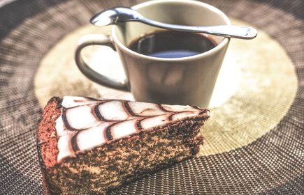 Stück Kuchen mit Marmormuster neben Tasse schwarzer Kaffee mit Löffel