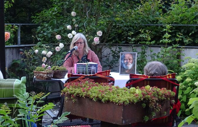 Vorlesende Frau am Mikrofon bei Gartenlesung im Grünen
