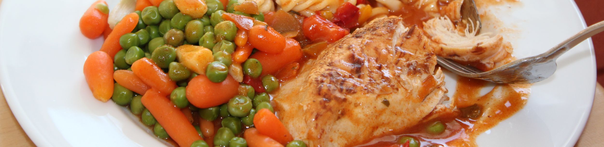 Teller mit Hähnchen, Spiralnudeln, Erbsen und Möhren beim Mittagstisch