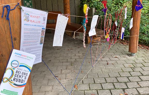 Offener Holzpavillon mit aufgereihten Kunstarbeiten und Flyer Kunst-Rallye