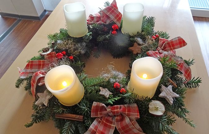 Adventskranz mit vier weißen Kerzen, roten Schleifen und Tannengrün