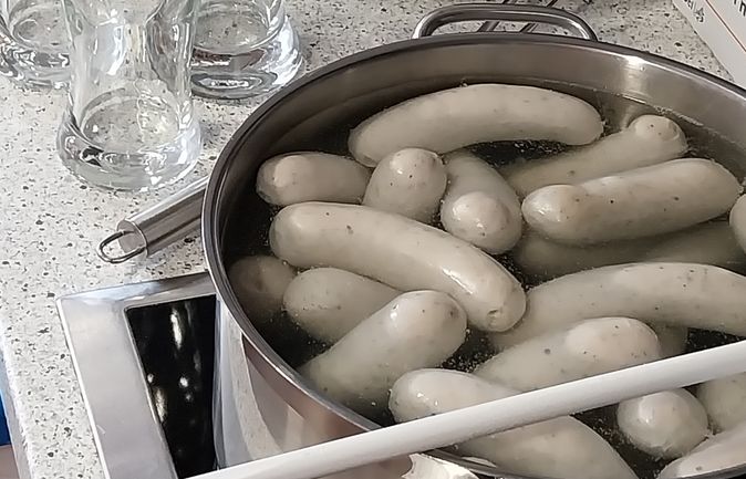 Gekochte Weißwürste im Topf neben Brezeln und Biergläsern