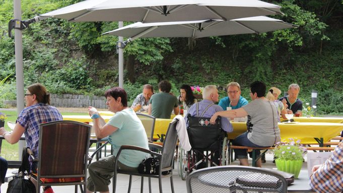 Senioren und Besucher sitzen im Café PAULA unter Sonnenschirmen