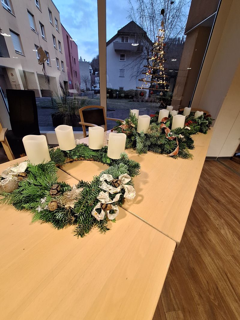 Adventkränze mit weißen Kerzen auf Tisch vor Fenster und beleuchteter Weihnachtsbaum draußen