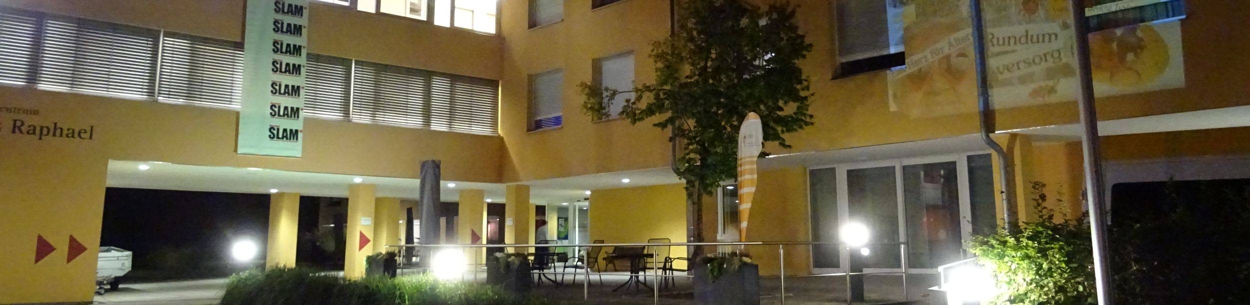 Bei Nacht beleuchtetes Gebäude mit SLAM-Banner und Fassadenprojektion