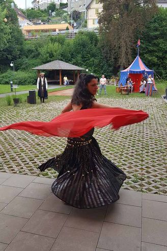 Tanzende Frau wirbelt rotes Tuch vor buntem Zelt
