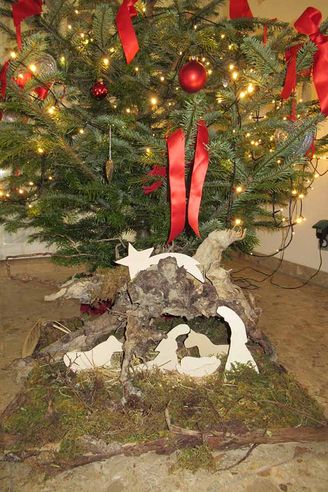 Weihnachtsbaum mit Lichterketten und Krippe aus Rindenstücken und weißen Figuren