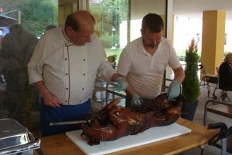 Zwei Männer tranchieren ein ganzes Spanferkel auf einem Tisch