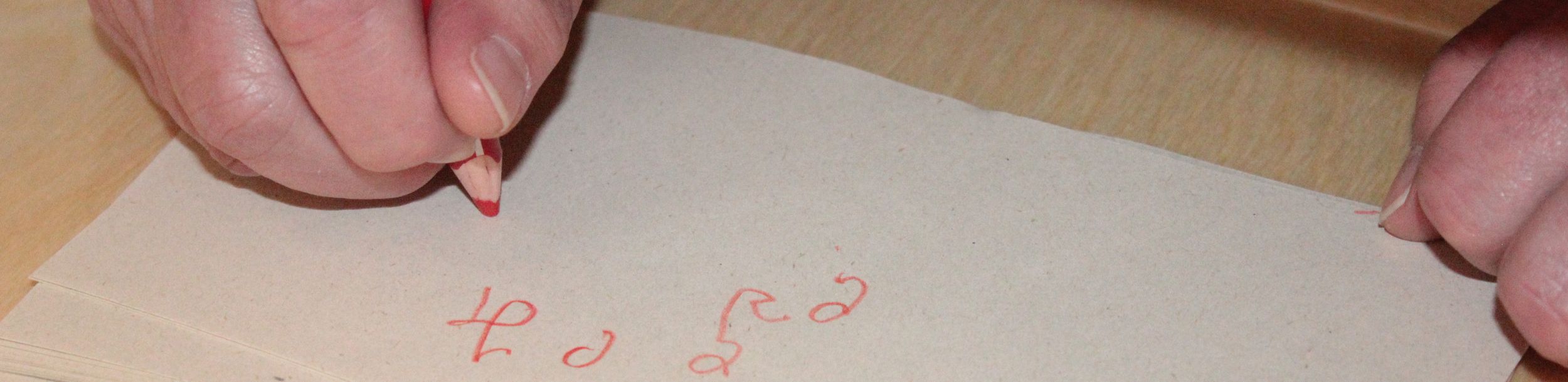 Hände schreiben mit rotem Buntstift auf Stapel hellgrauer Zettel
