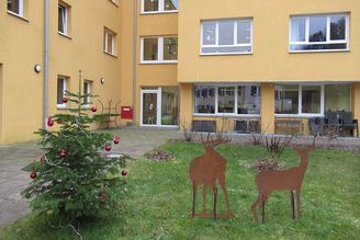 Geschmückter Tannenbaum und zwei rostige Metallfiguren in Hirschform vor Wohnhaus
