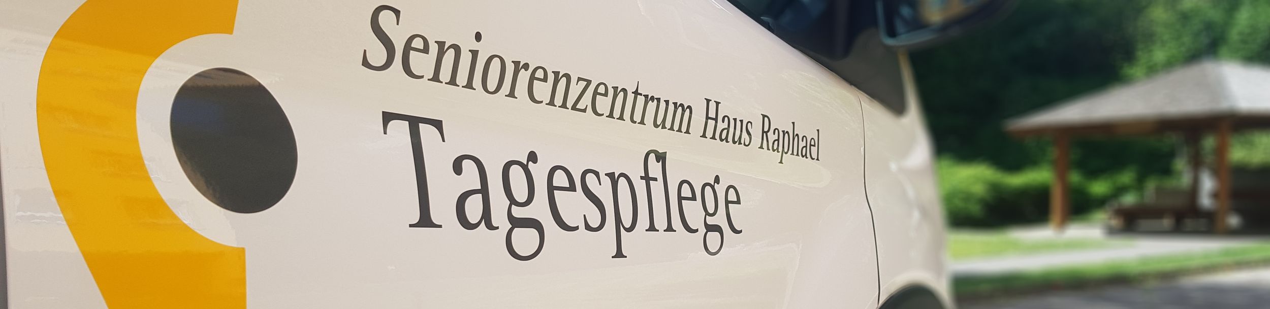 Fahrzeugtür mit Aufschrift Seniorenzentrum Haus Raphael Tagespflege und gelbem Logo