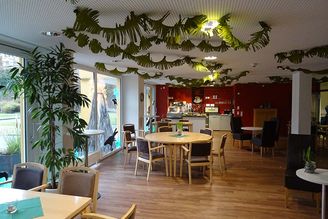 Gemeinschaftsraum mit runden Tischen, Stühlen, Tresen und Decken-Girlanden