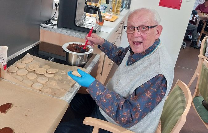 Senior in Tagespflege bestreicht Kekse mit Schokoglasur
