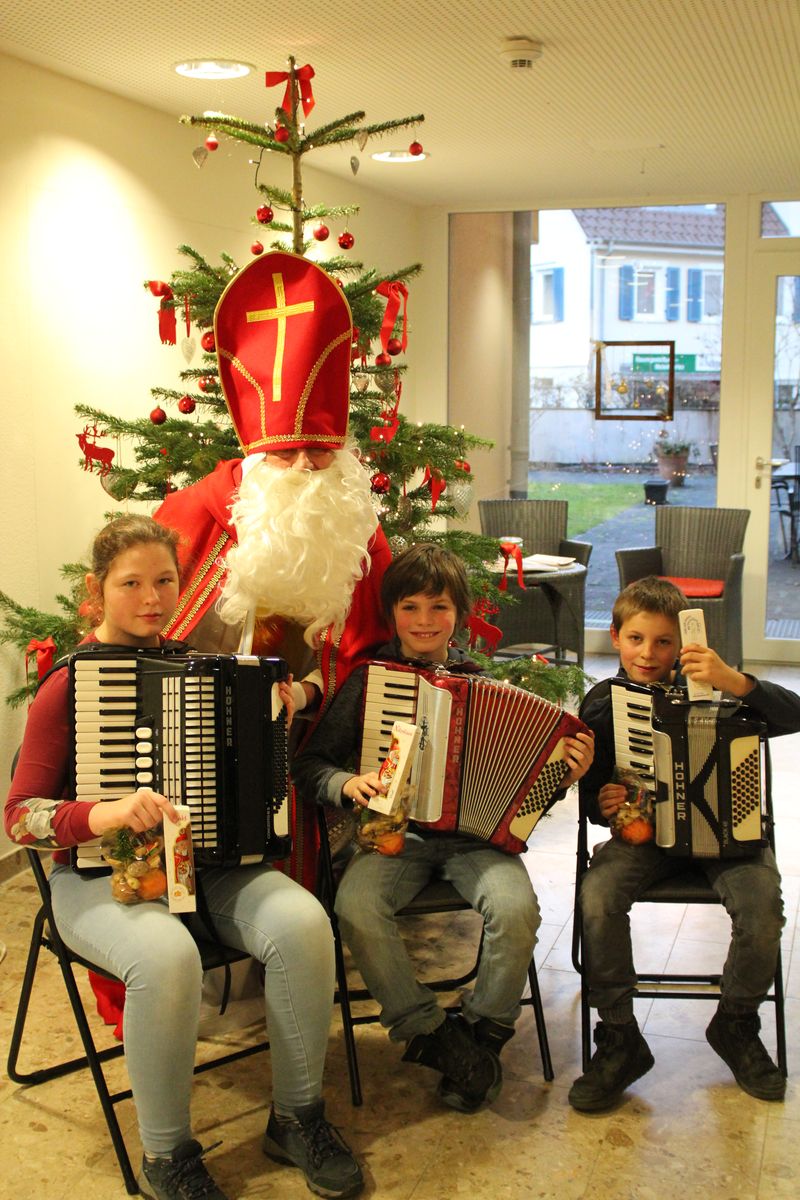 Kostümierter Nikolaus mit drei Kindern und Akkordeons vor geschmücktem Weihnachtsbaum
