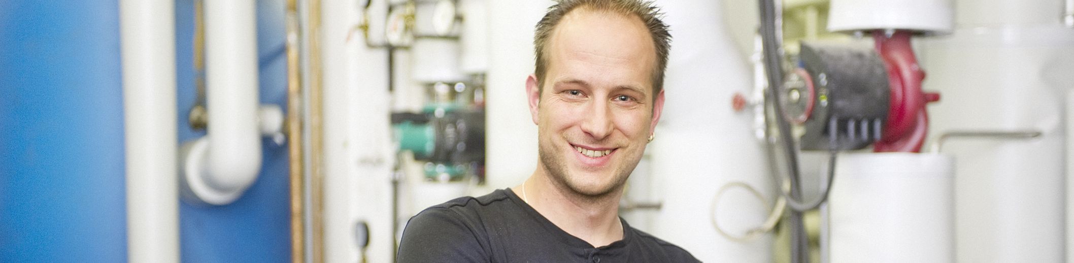 Mann mit verschränkten Armen lächelnd vor Rohrleitungen und Ventilen