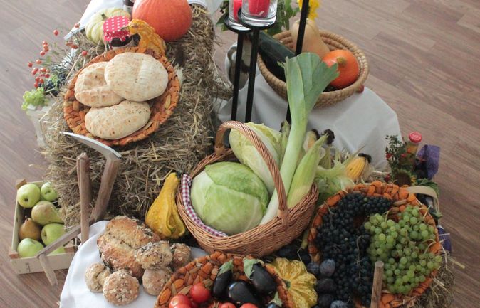 Erntedank-Tisch mit Körben voller Gemüse, Obst, Brot und Kerzen