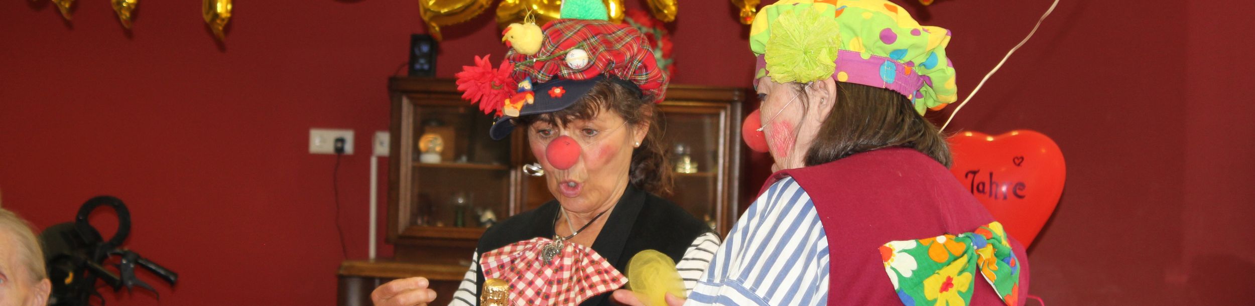 Zwei Clowns mit roten Nasen öffnen Champagner vor goldenen Geburtstagsballons